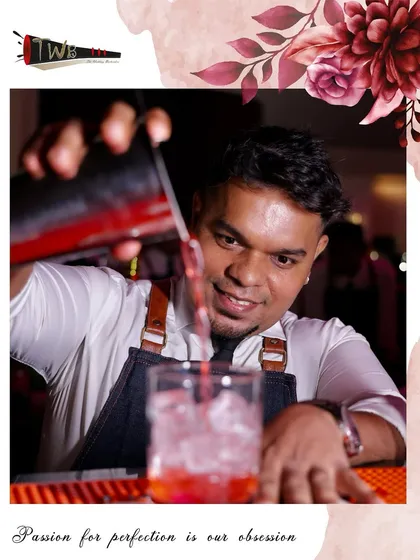 A smiling bartender pours a vibrant red cocktail, clearly enjoying the art of his craft.