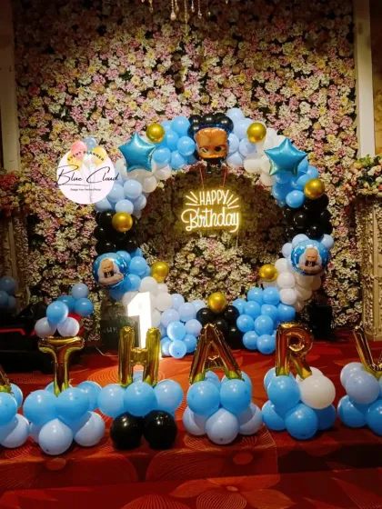A Boss Baby themed birthday setup with a blue, black, and gold balloon ring, neon sign, and balloon letters spelling the name 'ATHARV'.
