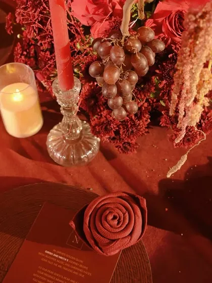 A place setting at the all-red reception dinner, with a napkin folded into a rose shape. The table is adorned with red flowers, grapes, and candles, creating a rich and immersive experience.