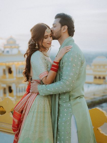 A tender moment as the groom kisses the bride's forehead on a palace balcony during their Mehendi event.