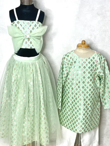 A soft mint green sibling set. This features a lehenga with a large bow detail for her and a matching printed kurta for him.