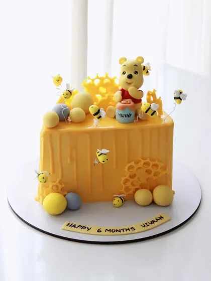 A Winnie the Pooh-themed cake for Vivaan's 6-month celebration, complete with a honey pot and buzzing bees.