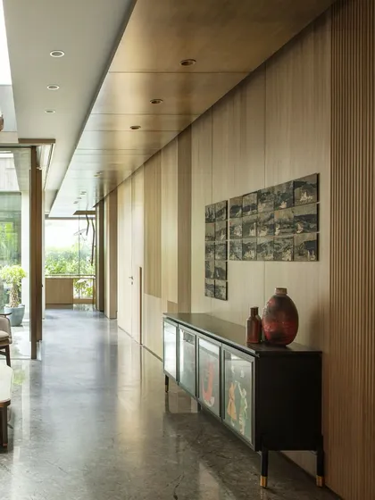 A long view of the family lounge corridor at the Bammi Residence. The aged brass ceiling and continuous wood paneling create a sense of warmth and flow, connecting different zones of the home.