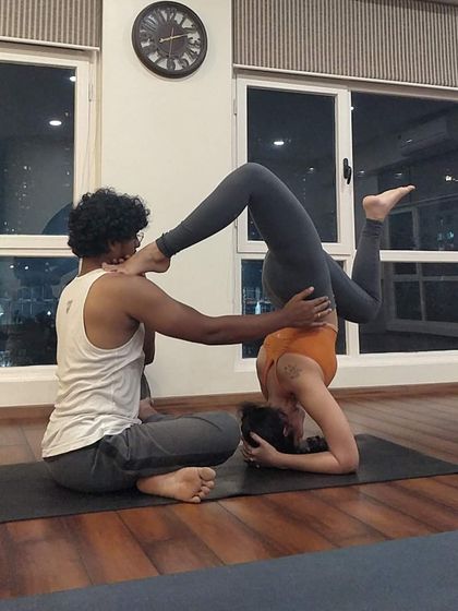 An instructor assists a student with a deep inversion, using his own body to provide a stable and supportive base.