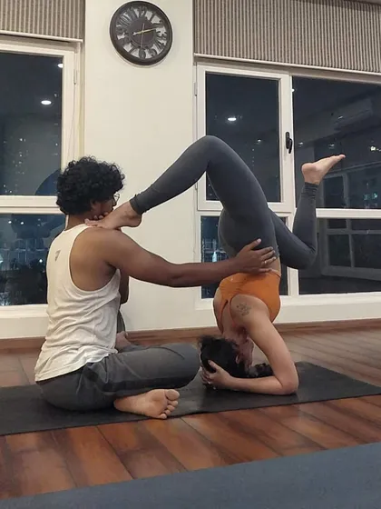 A creative and supportive adjustment in a variation of Sirsasana, or headstand. This partner-assisted stretch helps deepen the pose, demonstrating the trust and connection we foster between teachers and students.