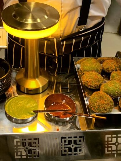 A server presenting a tray of hot Harabhara Kebabs, complete with mint and tamarind chutneys.