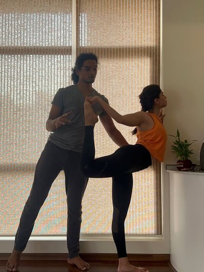 A student practices Natarajasana (Dancer's Pose) with wall support, a great way to work on the alignment and flexibility required for the full pose.