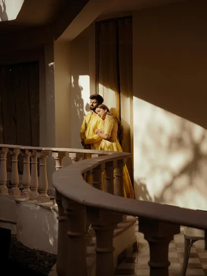 The couple shares a peaceful moment on a curved balcony, bathed in the golden hour light. The dramatic shadows and warm tones create a highly artistic and cinematic pre-wedding portrait.