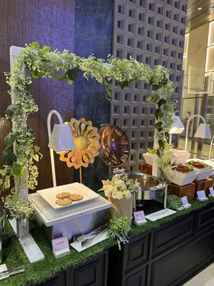 A fresh and airy buffet station framed by an arch of white and green foliage. This design brings a touch of nature indoors, creating a refreshing and vibrant atmosphere for daytime corporate events.