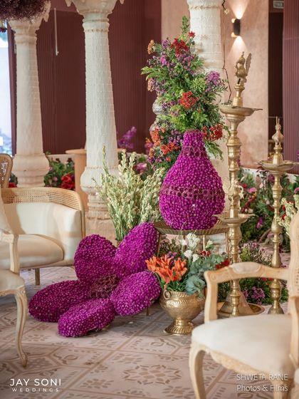 The sculptural purple flower arrangement seen in context, placed beside elegant white pillars and traditional brass lamps.