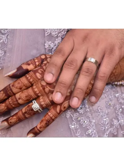 A symbol of commitment. The bride's henna-covered hand rests gently on her partner's, showcasing their beautiful engagement rings.