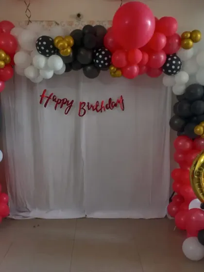 A simple birthday backdrop with a red, black, and white balloon arch over a white curtain.