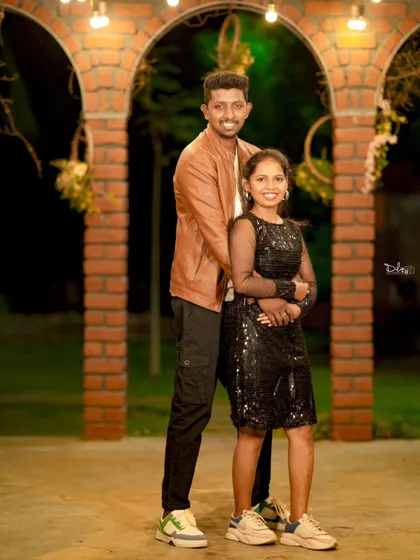 A full-length portrait of the couple under a lit brick archway. Their casual-chic outfits are perfect for this relaxed night shoot.