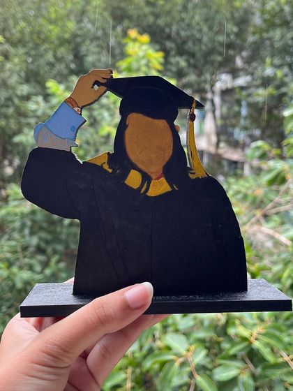 Celebrate a major milestone with a custom graduation miniature. This one features a faceless illustration style on a wooden cutout, complete with cap and gown.