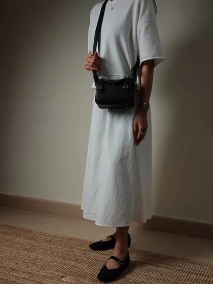 A full-body look at how the black Linde Mini can be styled with a simple white dress. It's a versatile bag that adds a touch of class to any minimalist outfit.