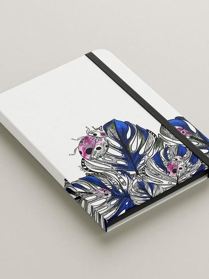 My ladybug illustration on the cover of a notebook. The design combines detailed black and white leaves with pops of colour on the ladybugs, making it a unique and artistic piece of stationery.