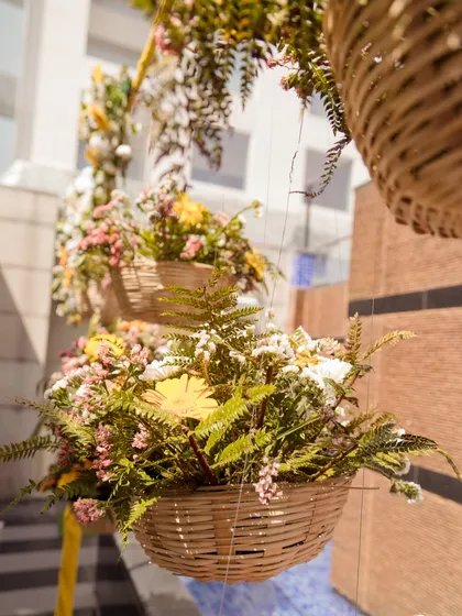 A close-up of the hanging floral baskets, filled with a mix of ferns and colorful flowers, adding a rustic charm to the Haldi decor.