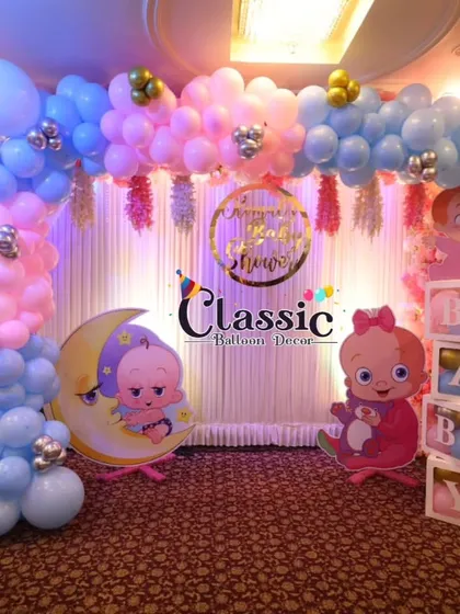 A beautiful baby shower stage setup in a hall, with a pastel balloon arch, a golden 'Baby Shower' sign, and charming baby-on-the-moon cutouts.