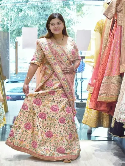 A happy customer trying on a beautiful floral embroidered lehenga in our store. The soft peach and pink tones make this a wonderful choice for a daytime wedding ceremony.