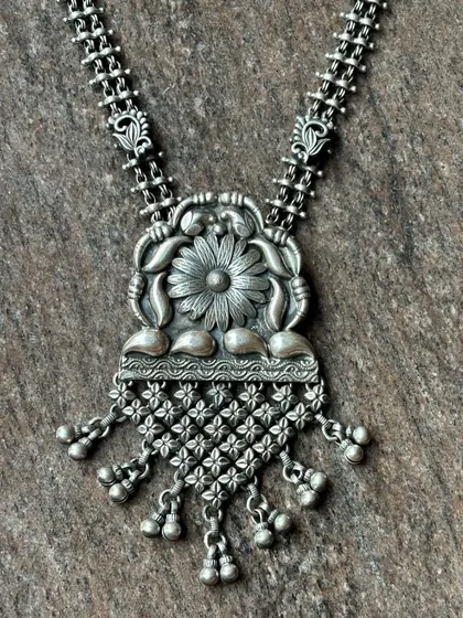 A unique oxidised silver pendant necklace. The pendant features a floral motif with a net-like jali drop, all on a detailed chain.