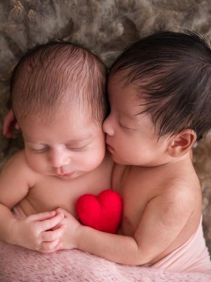 Sharing a heart from the very beginning. This pose with the tiny red heart symbolizes the inseparable bond between these newborn twins.