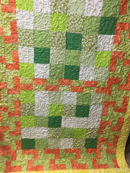 A close-up of a green and orange quilt with a textured, all-over quilting pattern.