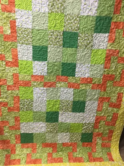 A close-up of a green and orange quilt with a textured, all-over quilting pattern.