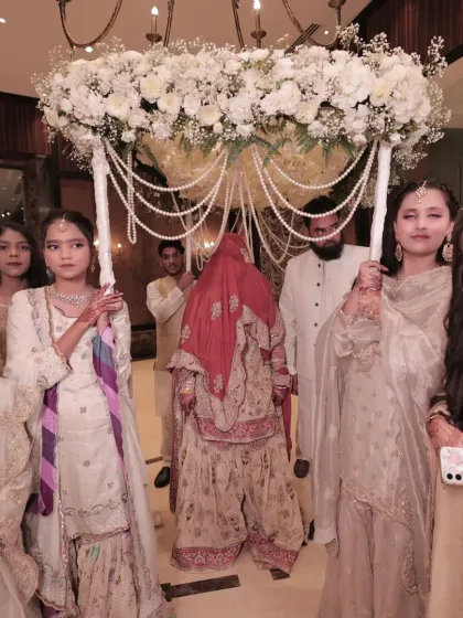 A traditional Nikah bridal entry. The bride is escorted under a stunning floral chaadar adorned with cascading pearls, blending cultural heritage with luxurious design.