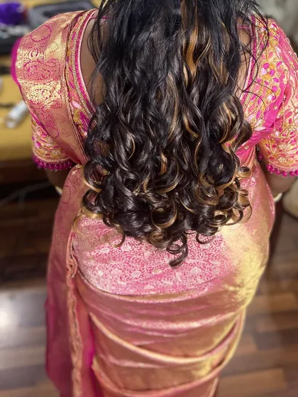 Beautifully styled curls with subtle highlights. This open hairstyle is perfect for a party or event, adding a touch of glamour to the traditional pink saree.