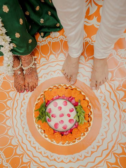 A symbolic shot from the Haldi ceremony, focusing on the couple's feet on the mandala-printed floor, with a decorated thali of haldi paste between them.