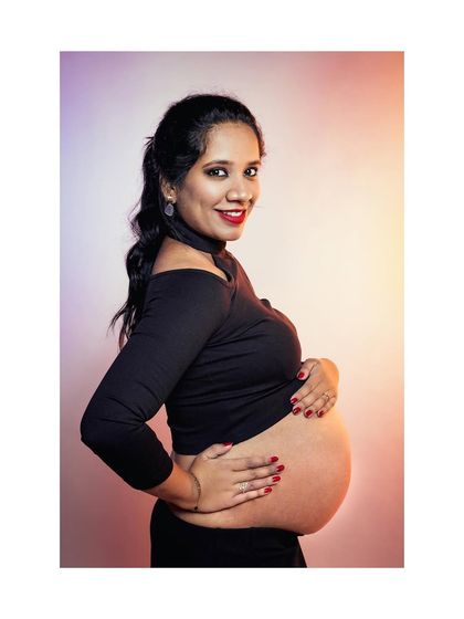A beautiful side-profile maternity portrait taken in our studio. The mother-to-be cradles her belly against a warm, colorful backdrop, emphasizing the beautiful curves of pregnancy.