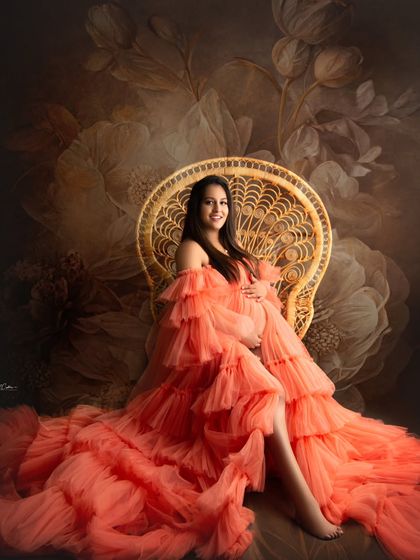 Seated on the peacock throne, this mom-to-be looks like royalty in her vibrant orange ruffled gown against a floral backdrop.