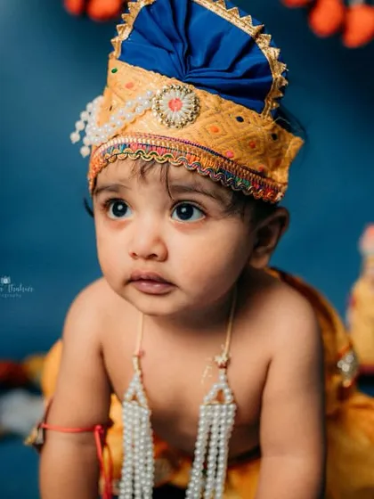 A thoughtful moment from our little Krishna. The rich blue background and peacock feathers create a beautiful, divine setting.