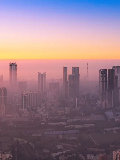 A closer view of Mumbai's skyscrapers piercing through the dense sunset haze, creating a layered and atmospheric cityscape.