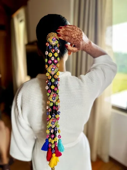 A getting-ready shot where the bride adjusts her hair, showing off the intricate details of the braid and her beautiful henna. It's a moment of quiet anticipation before the ceremony.