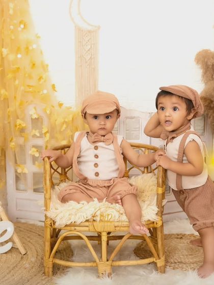 Twin boys in matching outfits pose for their first birthday shoot in a charming boho-themed setup.