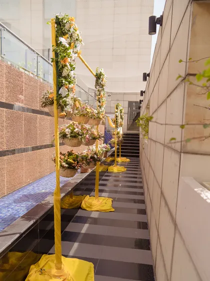 A floral aisle created with yellow stands holding baskets of fresh flowers, guiding guests along a poolside walkway.