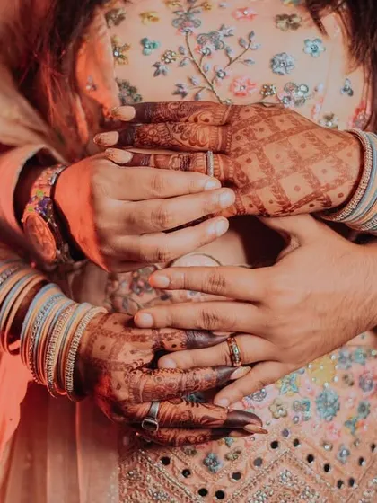 A creative close-up focusing on the couple's embrace and the details of their hands, showing the bride's bangles and the groom's ring.
