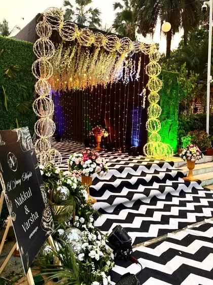 A unique photo booth or entrance for a modern reception. The design uses a black and white chevron carpet, a curtain of string lights, and an arch made of illuminated spheres.