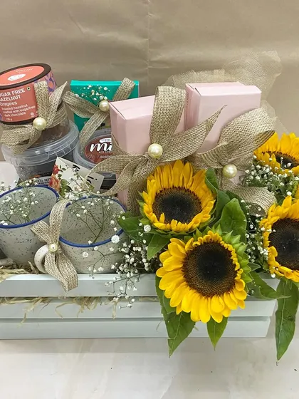 A Mother's Day surprise basket featuring bright sunflowers, custom mugs, and a selection of healthy and indulgent treats.