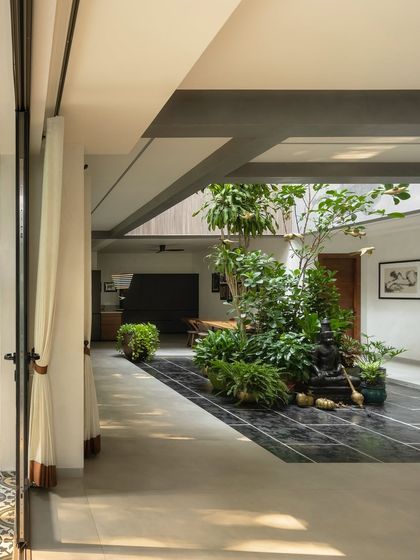 A view from a patterned tile patio into a home with a central green courtyard. The design creates a visual and physical connection between the outer garden and the inner sanctum, promoting a sense of continuous natural space.