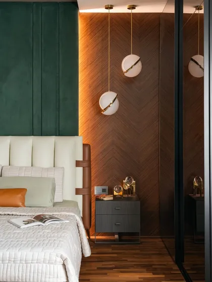 A detail of the master bedroom, where a dark green upholstered headboard contrasts with a chevron-patterned timber wall. The spherical pendant lights add a touch of sculptural elegance to the bedside.