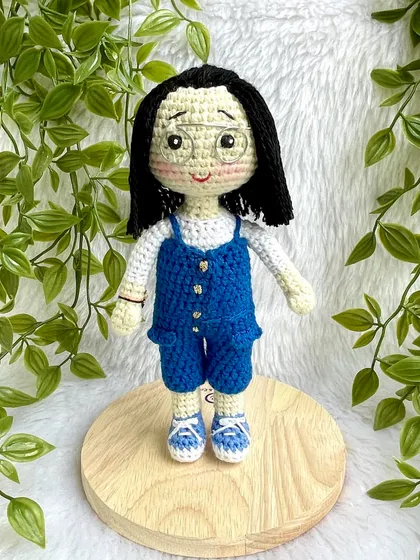 A lovely replica doll in a blue jumpsuit with matching shoes. The details, like her glasses and hairstyle, were carefully crafted to match the photos provided. These dolls can be made to stand on a wooden base.