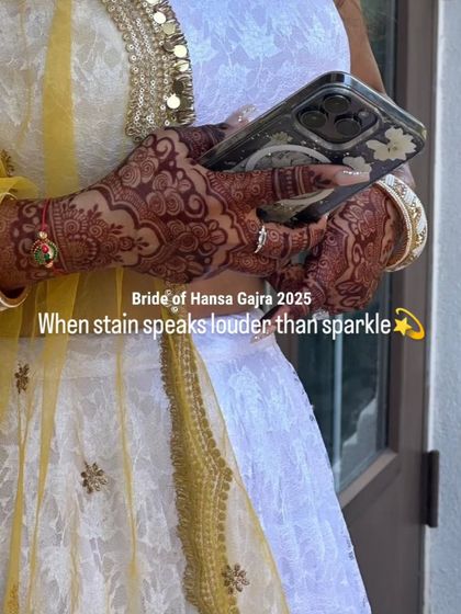 When the stain speaks louder than the sparkle. This photo shows the bride's beautifully stained hands against her elegant white and yellow outfit, proving that a rich henna color is the best accessory.
