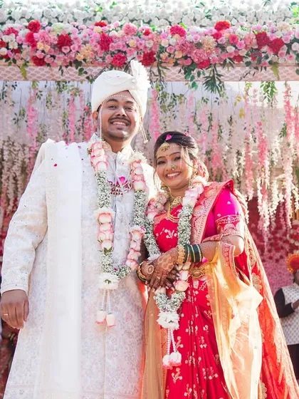 The happy couple under the mandap. Her makeup is designed to be picture-perfect, complementing the vibrant floral decor and her traditional attire.