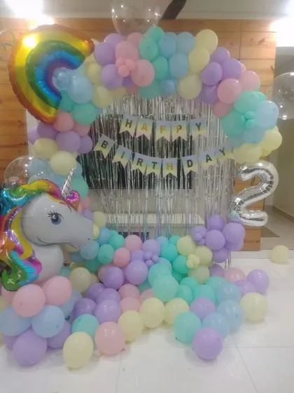 A dreamy unicorn-themed decoration for a 2nd birthday. We used a pastel rainbow balloon arch, a silver fringe curtain, and large unicorn and rainbow foil balloons to create a magical party space.