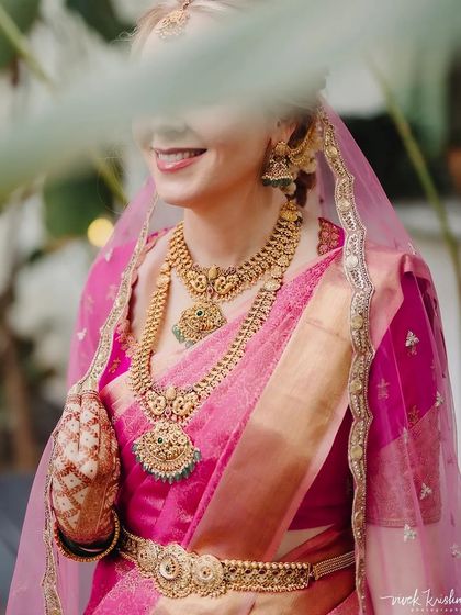 A candid shot of a smiling bride, her face partially hidden, drawing attention to her jewelry and stained henna.