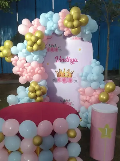 An outdoor princess-themed first birthday party with a pink and blue balloon arch and a custom backdrop.
