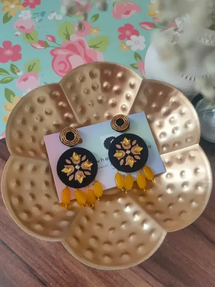 A pair of black fabric earrings with yellow floral embroidery and matching bead drops. The contrast of colors makes these a striking accessory for any occasion.