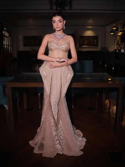 A full view of the champagne silk gown, showcasing its sculpted peplum details and the delicate, shimmering handwork on the fish-cut skirt.